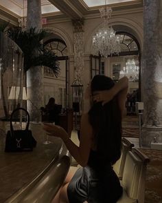 a woman sitting at a table in a hotel lobby with chandeliers hanging from the ceiling