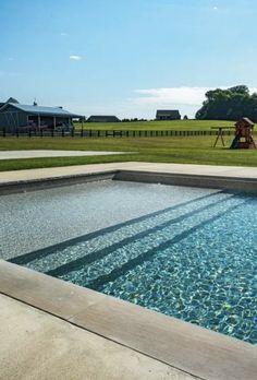 an empty swimming pool in the middle of a grassy area next to a horse farm