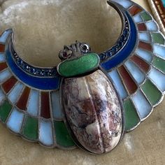 "Details: Plique-a-Jour Egyptian Revival Winged agate scarab brooch. The Plique-a-Jour colors range from deep green, red, white and blue. A simple agate scarab sits in the center, and the wings are edged in tiny blue stones of unknown origin--could even be glass(?). There is a hallmark stamped 900 and another that I can not make out stamped on the back. You will not be disappointed with this piece! Size: The piece measures 1 1/2\" wide and 1 1/8\" tall and weighs 12.6 grams. Condition: The overa Multicolor Cabochon Brooches For Collectors, Unique Oval Cabochon Brooches, Collectible Art Deco Cabochon Brooches, Art Deco Cabochon Brooches Collectible, Artisan Collectible Jewelry Brooch, Unique Multicolor Cabochon Brooches, Handmade Art Deco Collectible Brooch, Handmade Art Deco Collectible Brooches, Unique Gemstone Pendant Brooch