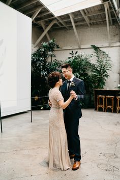 a man and woman standing next to each other in front of a plant filled wall