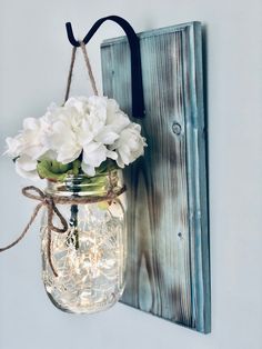 a mason jar filled with white flowers hanging from a wall