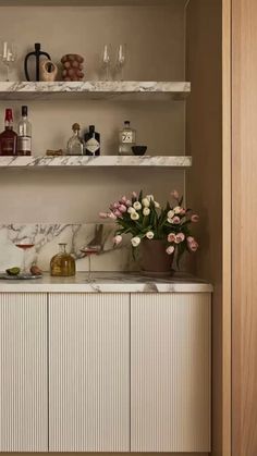 a kitchen with marble counter tops and shelves filled with bottles, glasses, and vases