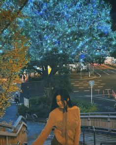 a woman walking up some stairs in front of a tree with blue lights on it