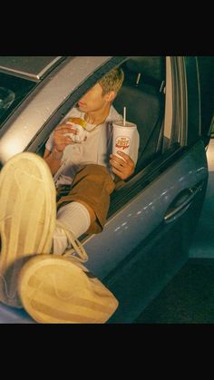 a man sitting in the back seat of a car while holding a drink and eating