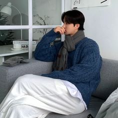 a person sitting on a couch with a blanket over their head and a scarf around his neck