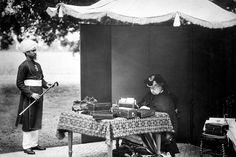 an old photo of two men sitting at a table in front of a tent with boxes on it