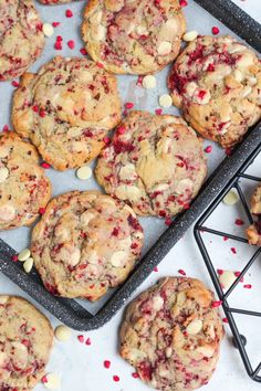 cookies with white chocolate chips and cranberries are on a baking sheet next to a cooling rack