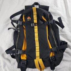 a black and yellow backpack sitting on top of a white sheet