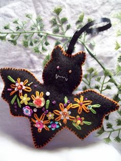 an embroidered bat ornament with flowers on it's back sits on a white surface