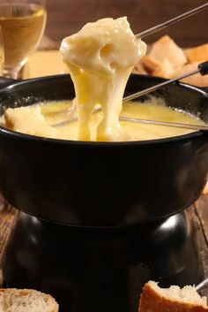 a black bowl filled with cheese and bread on top of a table next to wine glasses