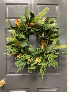 a wreath on the front door of a house with green leaves and gold ribbon hanging from it