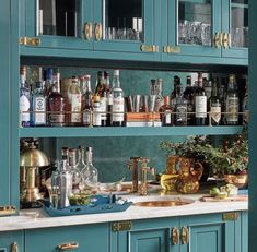 a kitchen with blue cabinets and gold pulls on the cupboards is filled with liquor bottles