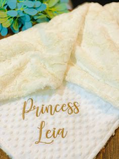 a white towel with the word princess leia written in gold on it next to a blue flower