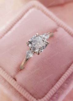 an engagement ring with three pear shaped diamonds in a pink velvet box on top of it