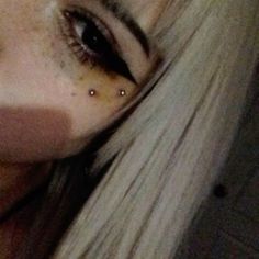 a woman with long blonde hair and piercings on her nose looking at the camera