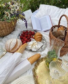 a table topped with bread and fruit next to a basket filled with strawberries on top of a white blanket