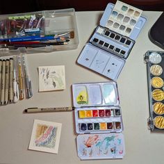 an assortment of watercolors and other art supplies on a table with pens, pencils, markers and cards