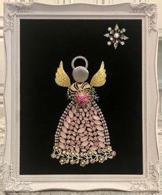 an angel made out of buttons and beads on a black background with a white frame