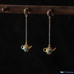 two gold teapots hanging from chains on a black background, one has a blue bead in the middle