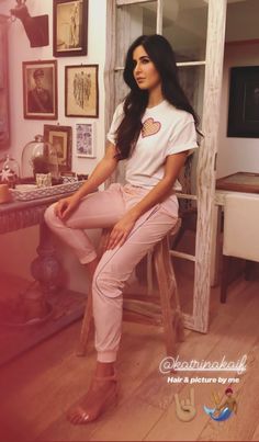 a woman sitting on top of a wooden stool in front of a desk with pictures