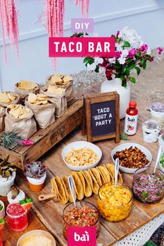 an assortment of taco bar food on a wooden table with pink flowers in the background