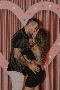 a man and woman kissing in front of a heart - shaped backdrop with lights on it