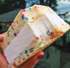 someone holding up a piece of cake with white frosting and sprinkles