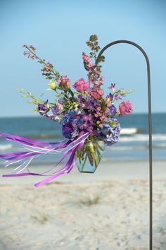 a vase filled with purple flowers sitting on top of a beach