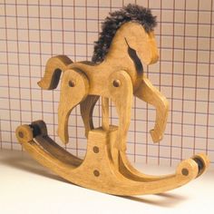 a wooden rocking horse with black hair on it's head and tail, sitting in front of a tiled wall