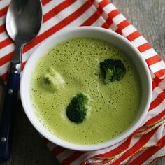 a bowl of broccoli soup on a red and white striped napkin with a spoon