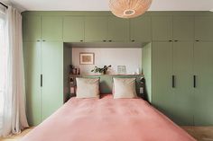 a bed with pink sheets and pillows in a green room