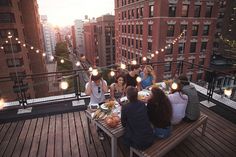 a group of people sitting at a table on top of a building with lights strung above them