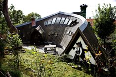 an unusual house is in the middle of some trees and grass, with a bench near it