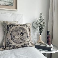 a white bed topped with two pillows next to a vase filled with flowers and plants