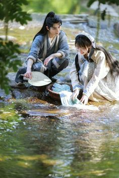 two people are sitting in the water with frisbees and one is holding something