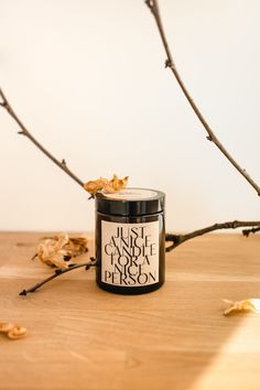 a candle sitting on top of a wooden table next to some branches and leaves in front of a white wall