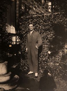 an old black and white photo of a man standing in front of a ivy covered building