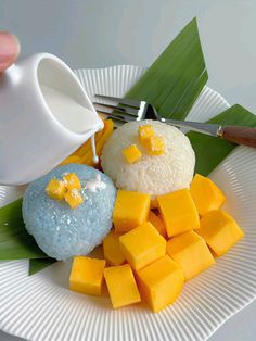 a white plate topped with rice and mangoes next to a cup filled with milk