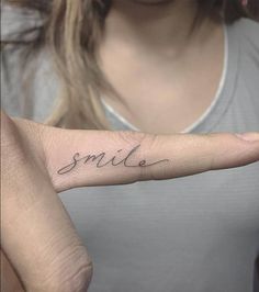 a woman with a small smile tattoo on her left hand and the word smile written in cursive font