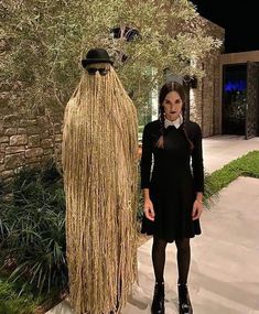 a woman standing in front of a giant fake grass man with glasses on his head