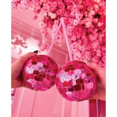 two pink disco ball ornaments hanging from a string in front of a flowery wall