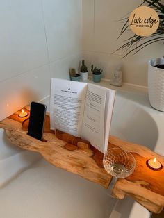 an open book sitting on top of a bath tub next to candles and a phone