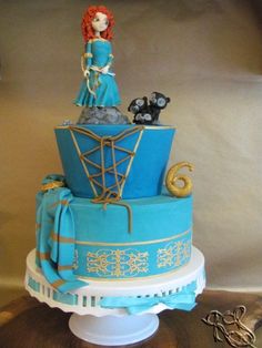 there is a blue and gold cake with a woman on top that has cats sitting on it