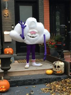 a large white cloud mascot standing on the front steps of a house with pumpkins around it