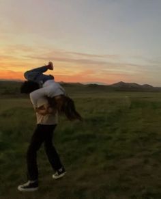 two people are standing in a field with the sun setting behind them and one person is upside down