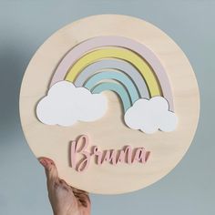 a person holding up a wooden sign with a rainbow and clouds on it that says mama