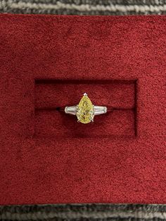 a yellow diamond ring sitting on top of a red velvet box with a silver band