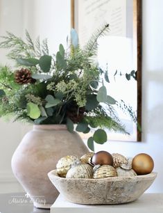 a white vase filled with christmas ornaments on top of a table next to a potted plant