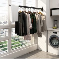 a washing machine sitting next to a window with clothes hanging on the rack in front of it