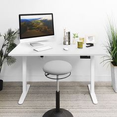 a white desk with a computer monitor and keyboard sitting on top of it next to potted plants